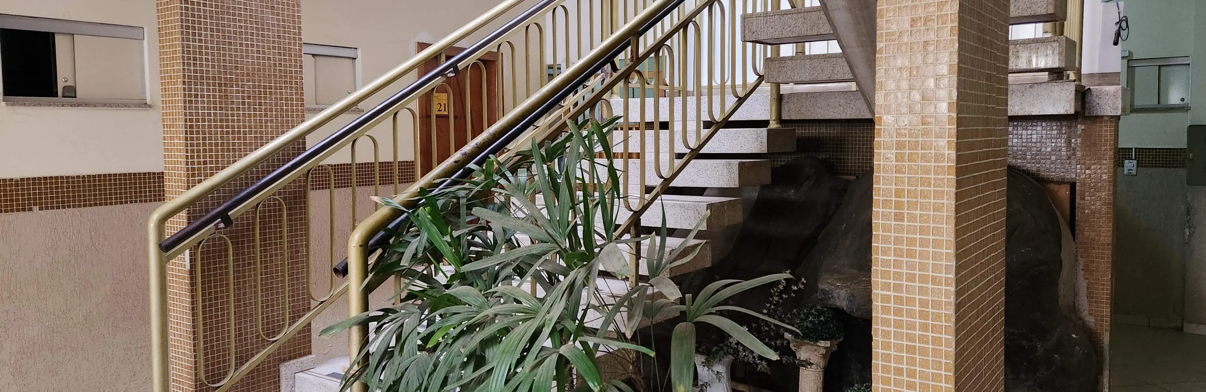 imagem da escada com plantas que da acesso ao andar de cima do hotel, e com visão para a porta do quarto 121